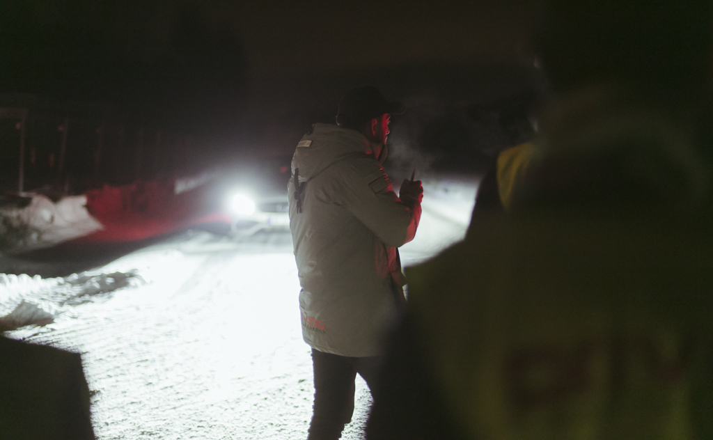 Bildet er tatt ute i mørket en vinterkveld. Trafikkskole elever står og ser imens en bil med fjernlys står foran mot de.